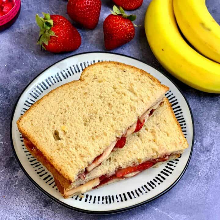fruit sandwich served on a plate with strawberry and banana on side