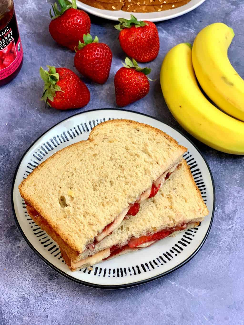 fruit sandwich cut into half served on a plate with strawberries and banana on the side