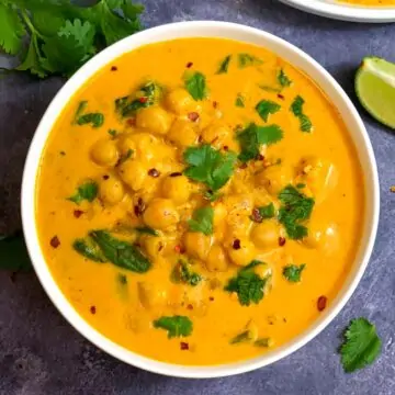 Chickpea Coconut Curry mde of coconut milk and chickpeas served in a bowl garnished with chilli flakes and cilantro with a side of lemon