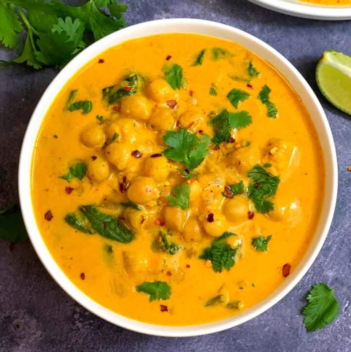 Chickpea Coconut Curry made of coconut milk and chickpeas served in a bowl garnished with chilli flakes and cilantro with a side of lemon