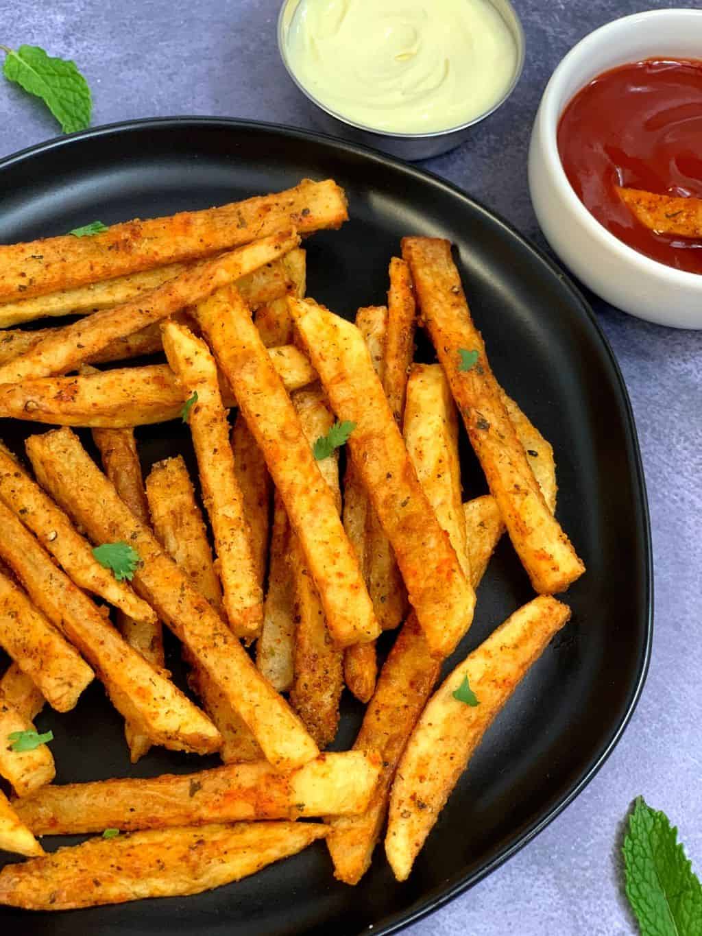 masala french fries served on a plate along with ketchup and mayonnaise