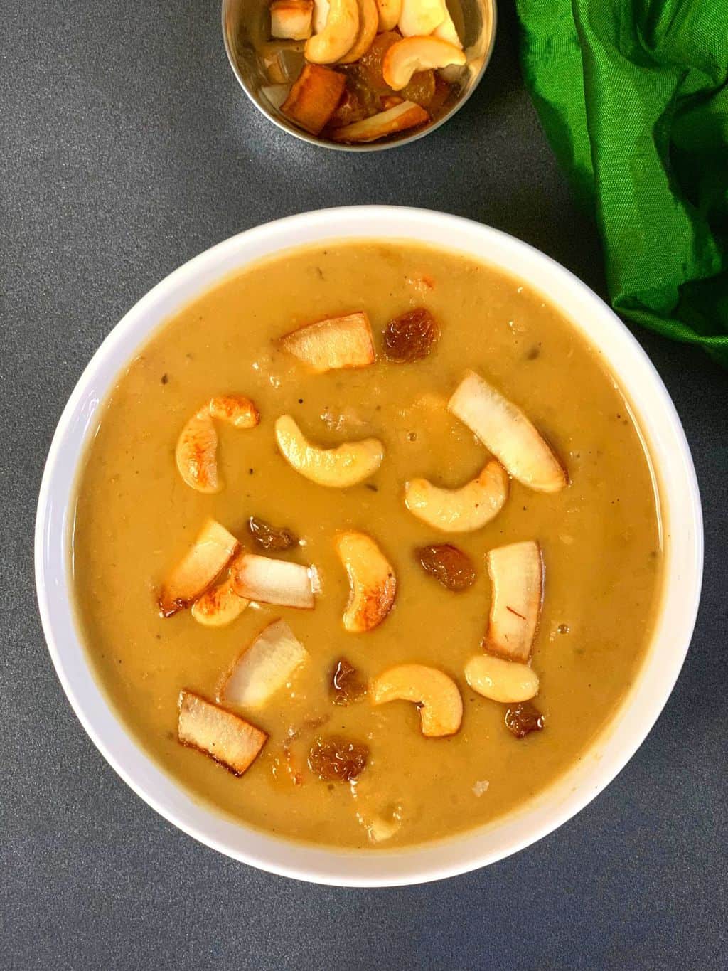 moong dal payasam served in a bowl garnished with roasted nuts and coconut and on the side a cup with roasted nuts