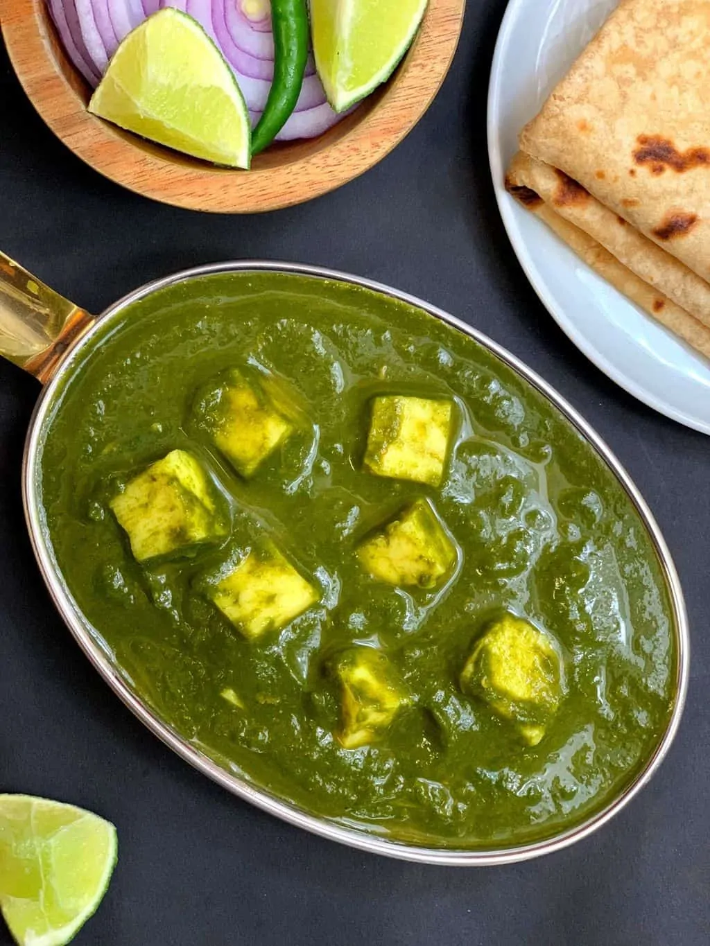 instant pot palak paneer served in a copper bottom serving dish with chapati and lemon on side