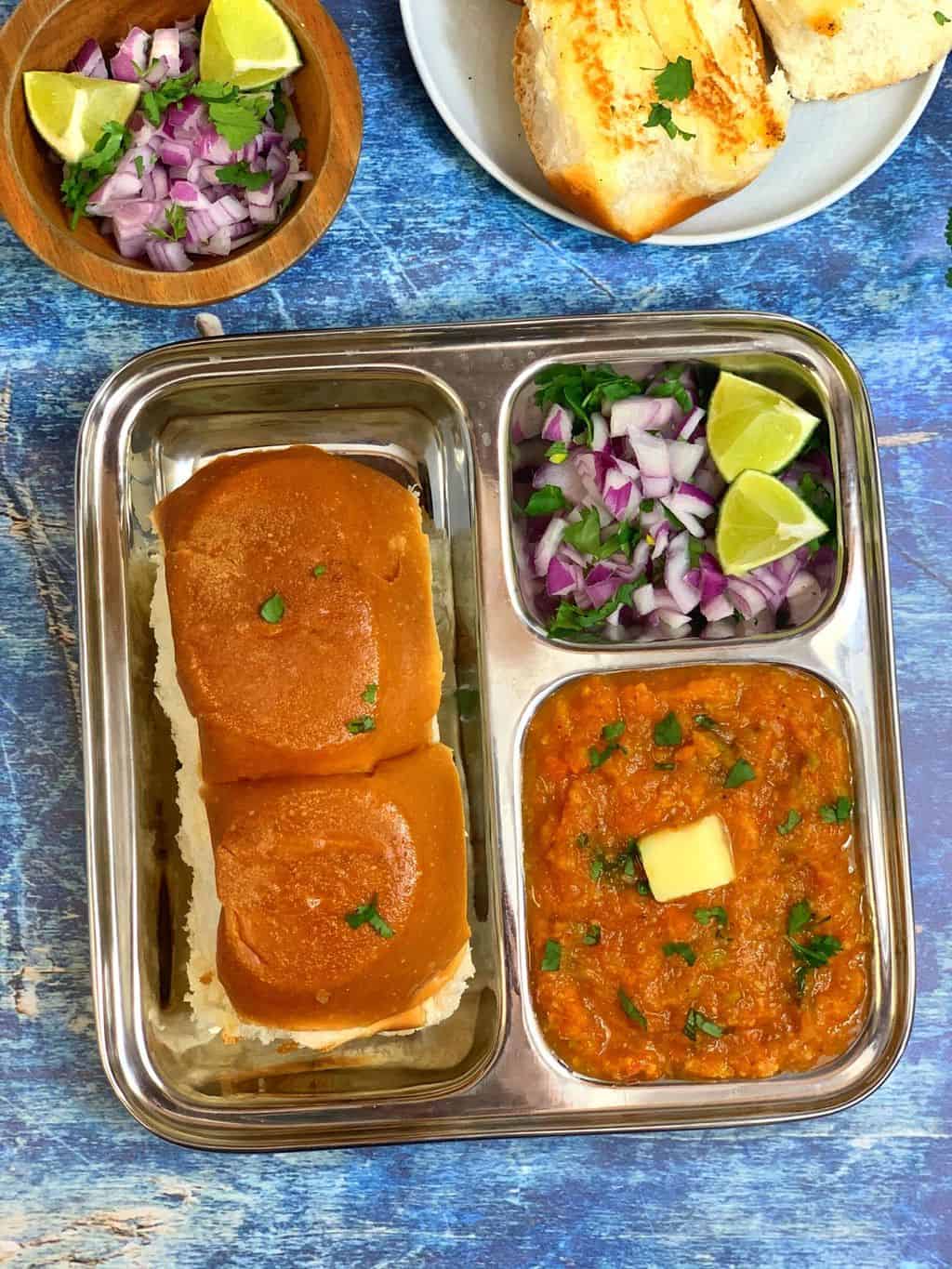 pav bhaji served in a plate with pav and onions and lemon wedges
