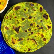 spinach paratha on black sheet with cabbage curry and pickle on side