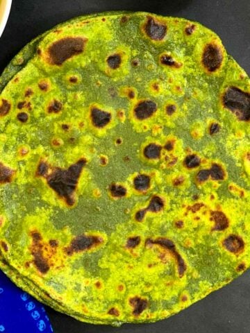 spinach paratha on black sheet with cabbage curry on side