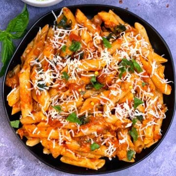 Tomato Basil Pasta served in a plate topped with cheese and basil