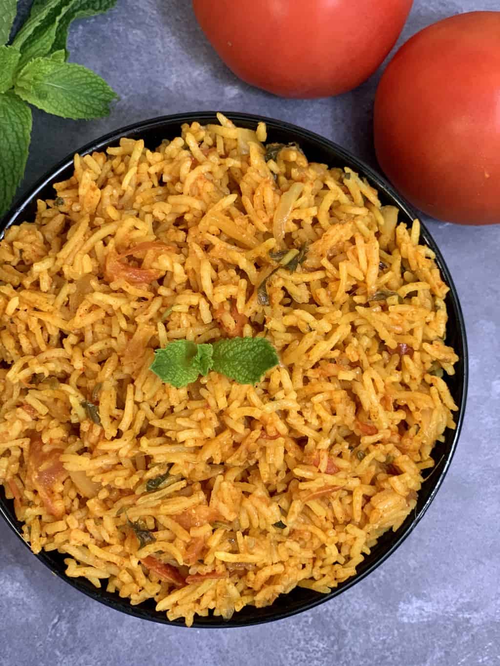 instant pot tomato rice made with coconut milk served in a black bowl and raw whole tomatoes on the side