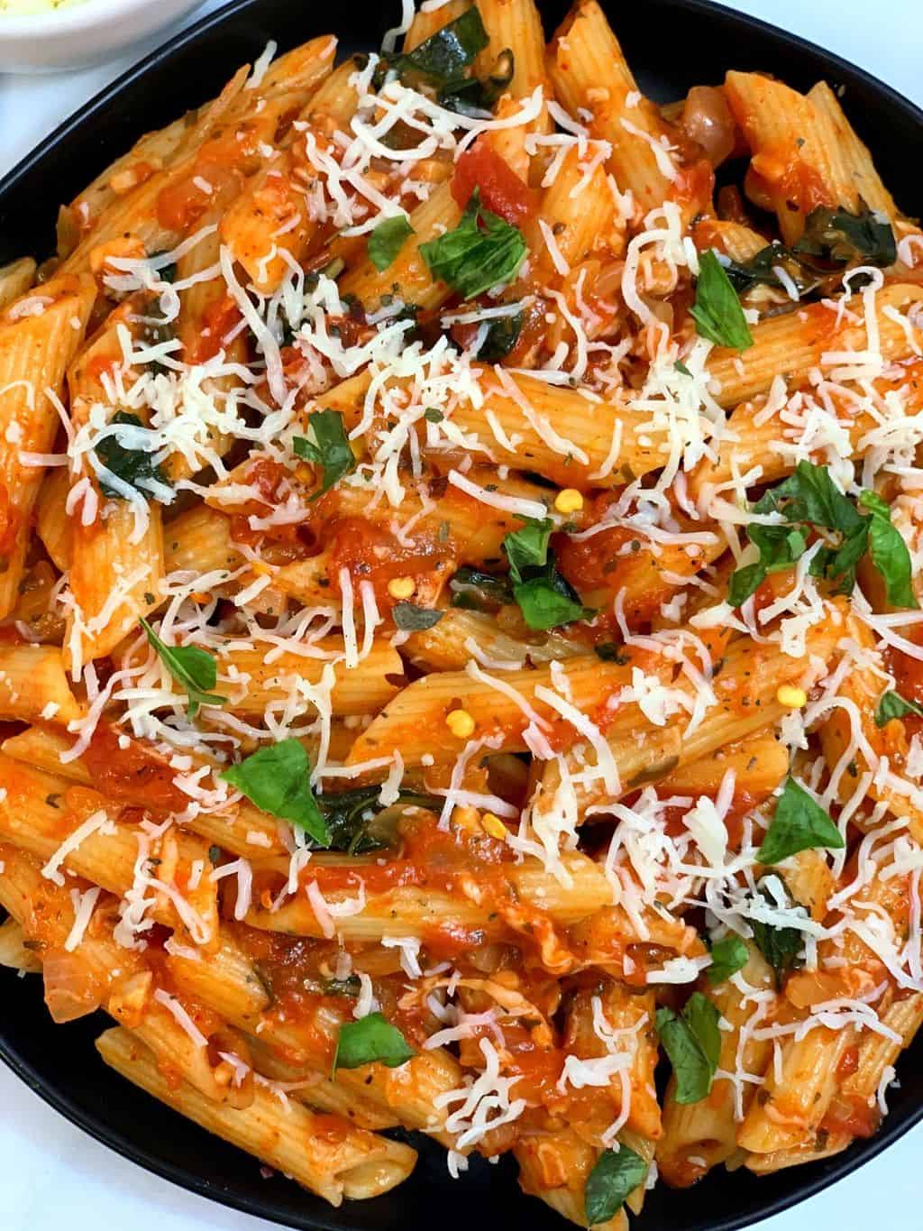 tomato basil pasta served in a plate garnished with cheese and basil leaves