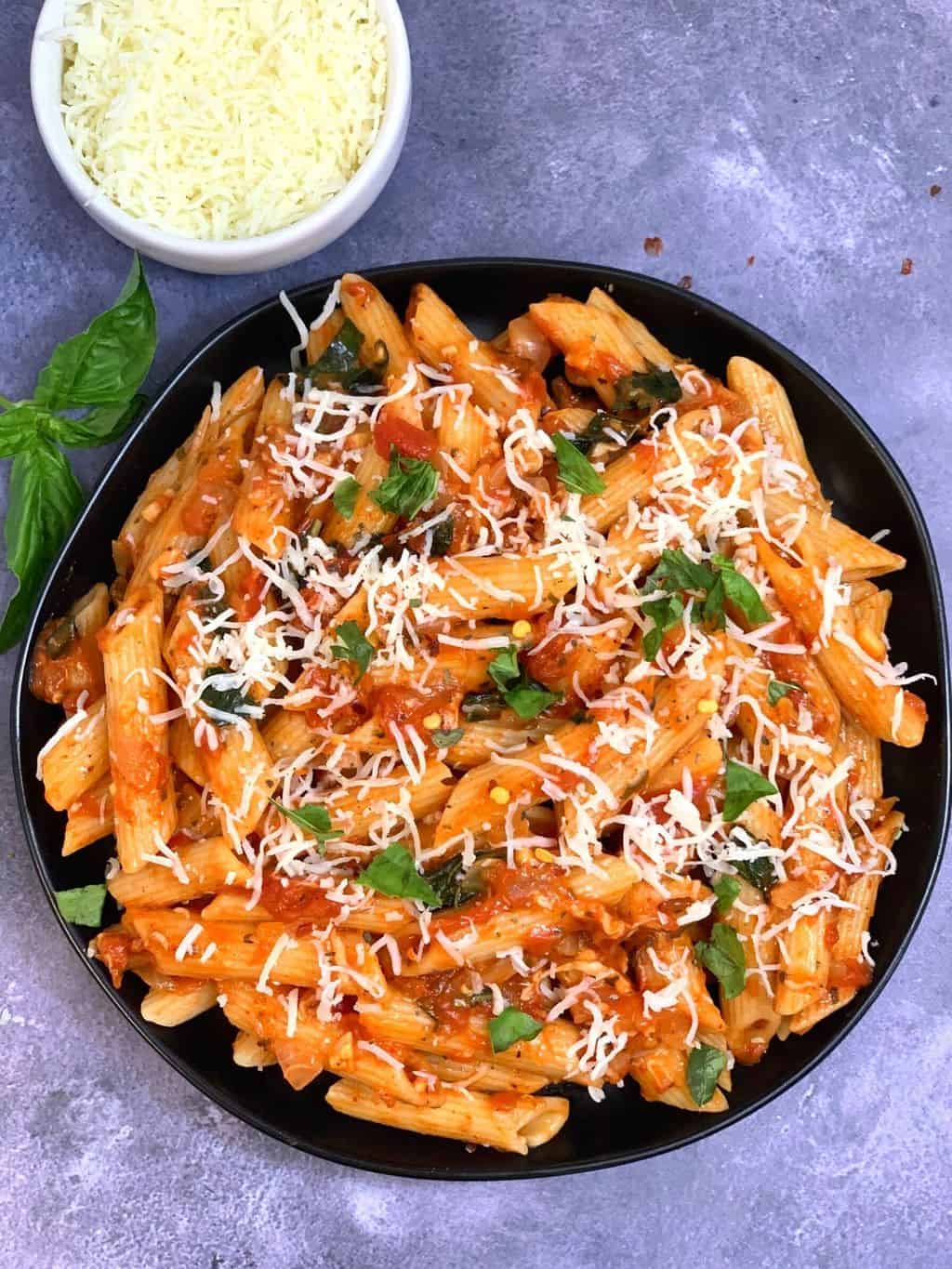 Tomato Basil Pasta served in a plate garnished with basil and cheese