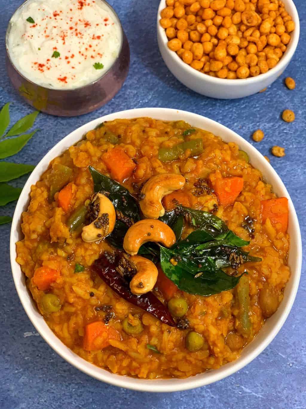 Instant Pot Bisibelebath/bisi bele bath recipe served in a white bowl ,boondi and raita on side