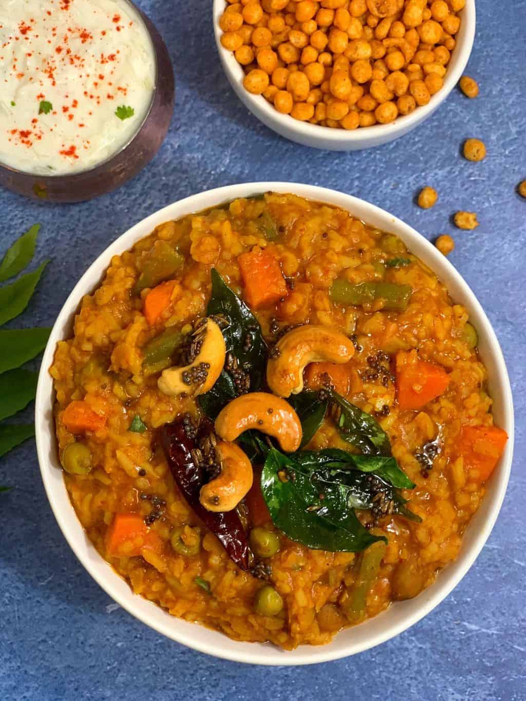 instant pot bisibelebath served in a bowl with boondi and raita on the side