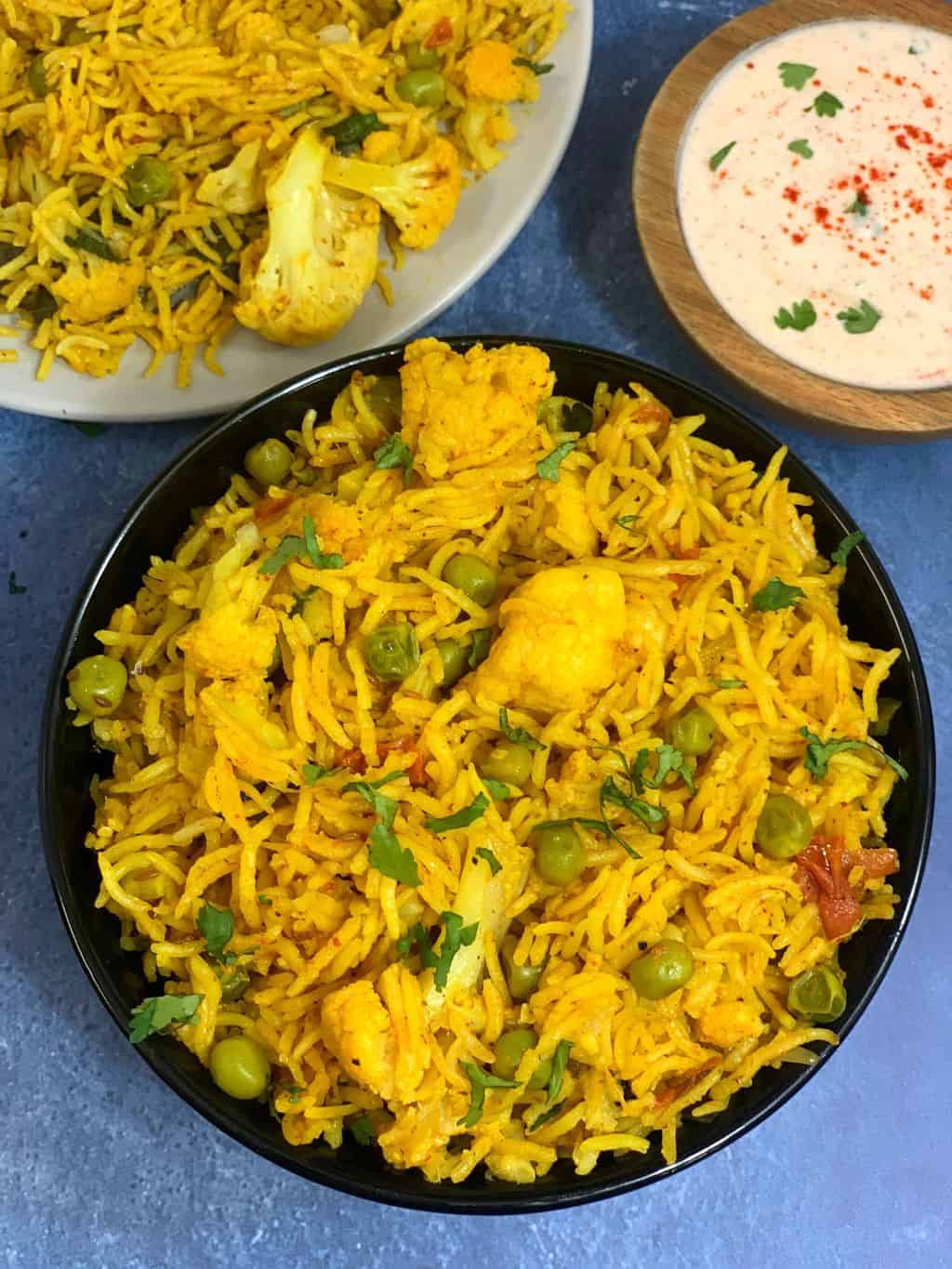 Cauliflower Pulao in a black bowl with some raita on side