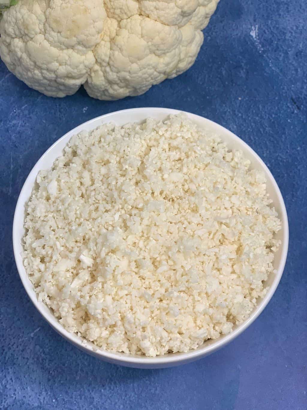 cauliflower rice served in a bowl with whole cauliflower on the side