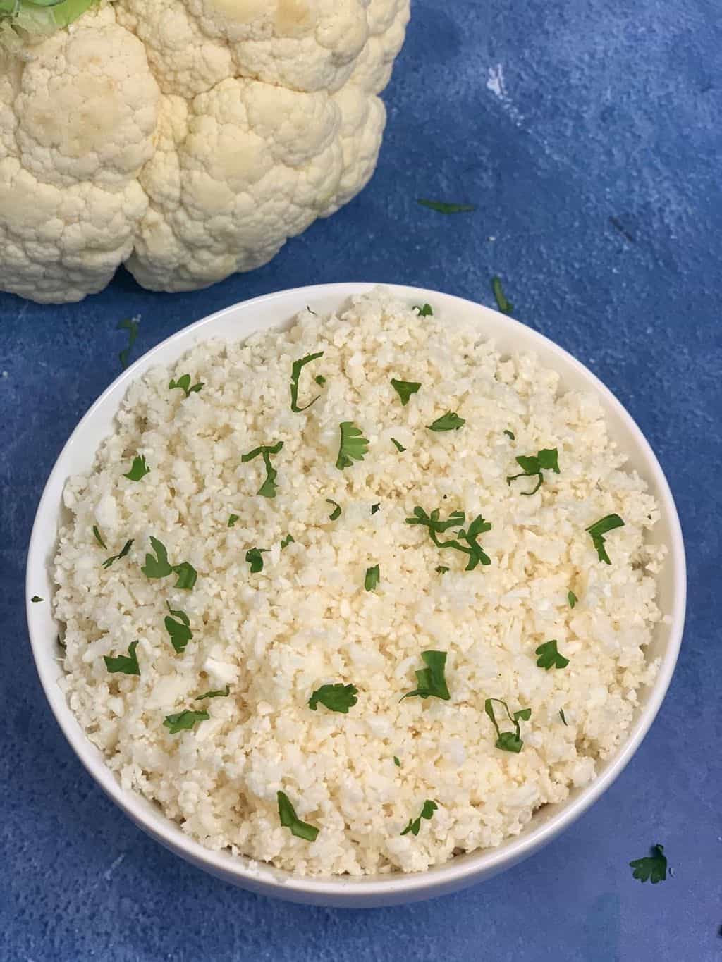 cauliflower rice served in a bowl garnished with cilantro and whole cauliflower on the side