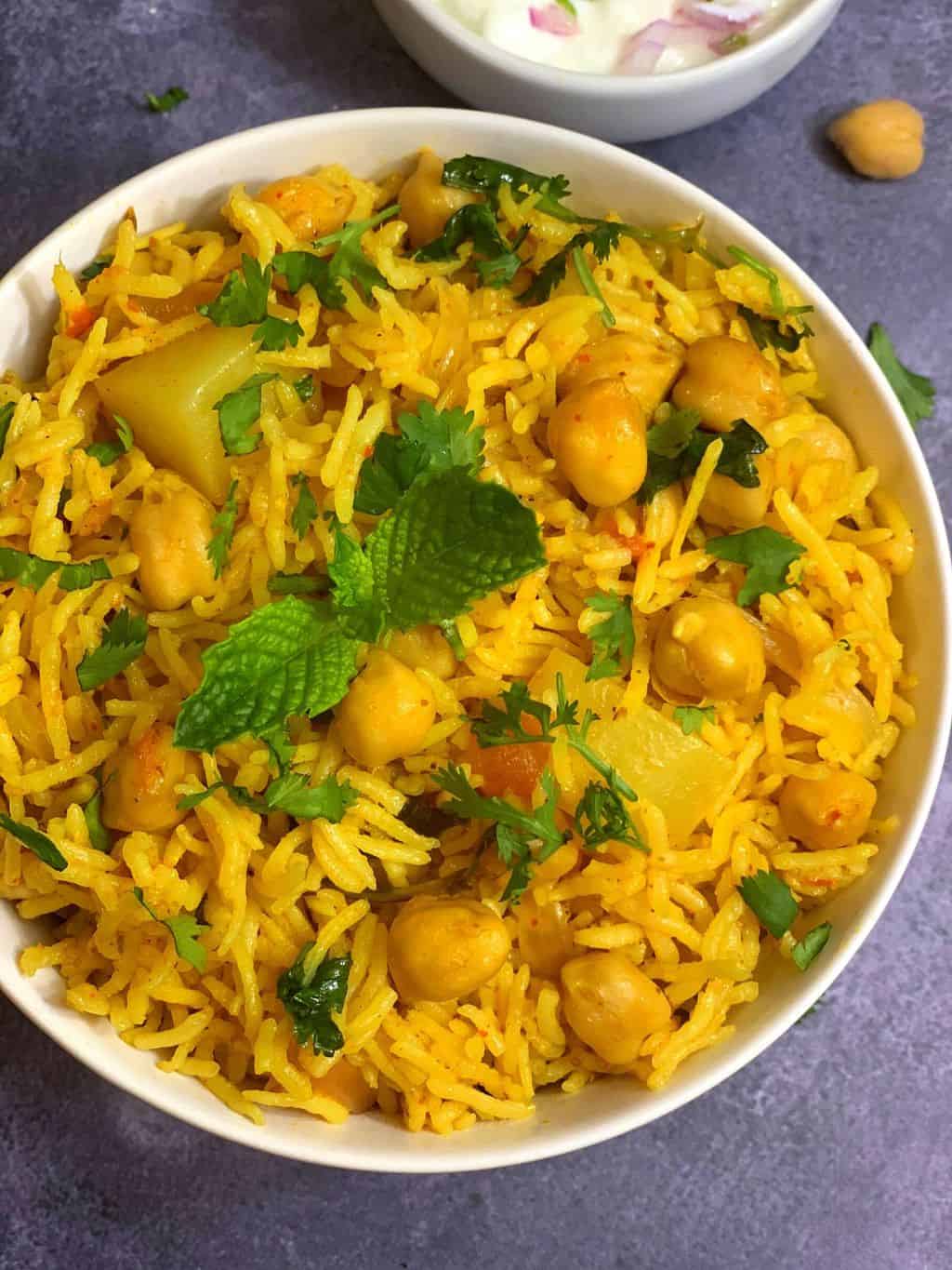 chickpea biryani served in a bowl garnished with mint and boondi raita on the side