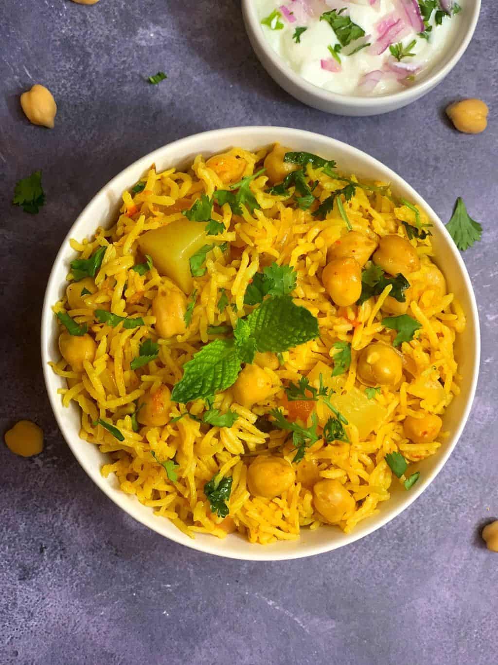 chole pulao served in a bowl garnished with mint with side of raita