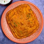 A stack of Dal parathas on a serving plate with raita on side
