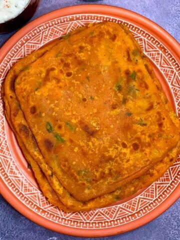 A stack of Dal parathas on a serving plate with raita on side