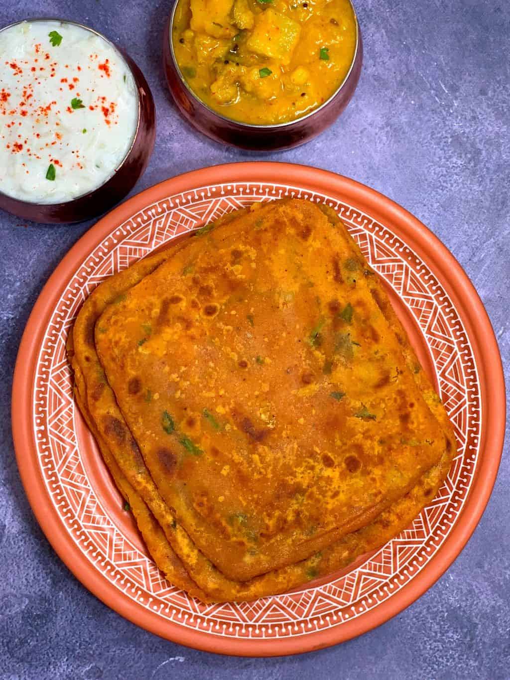 dal paratha stacked on a plate with side of raita and dal