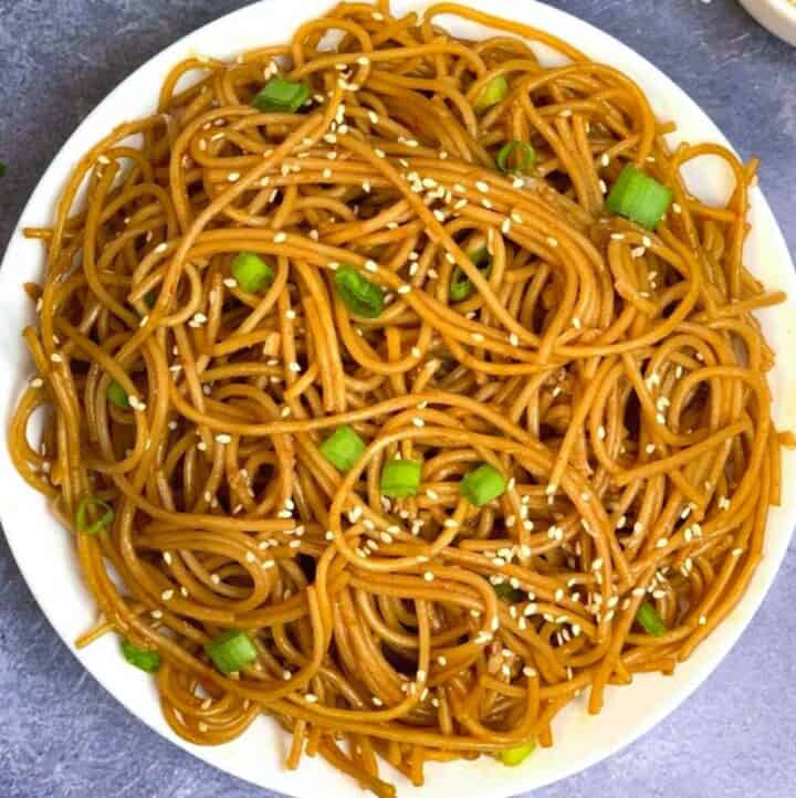 Garlic Noodles served in a white plate garnished with sesame seeds and green onions