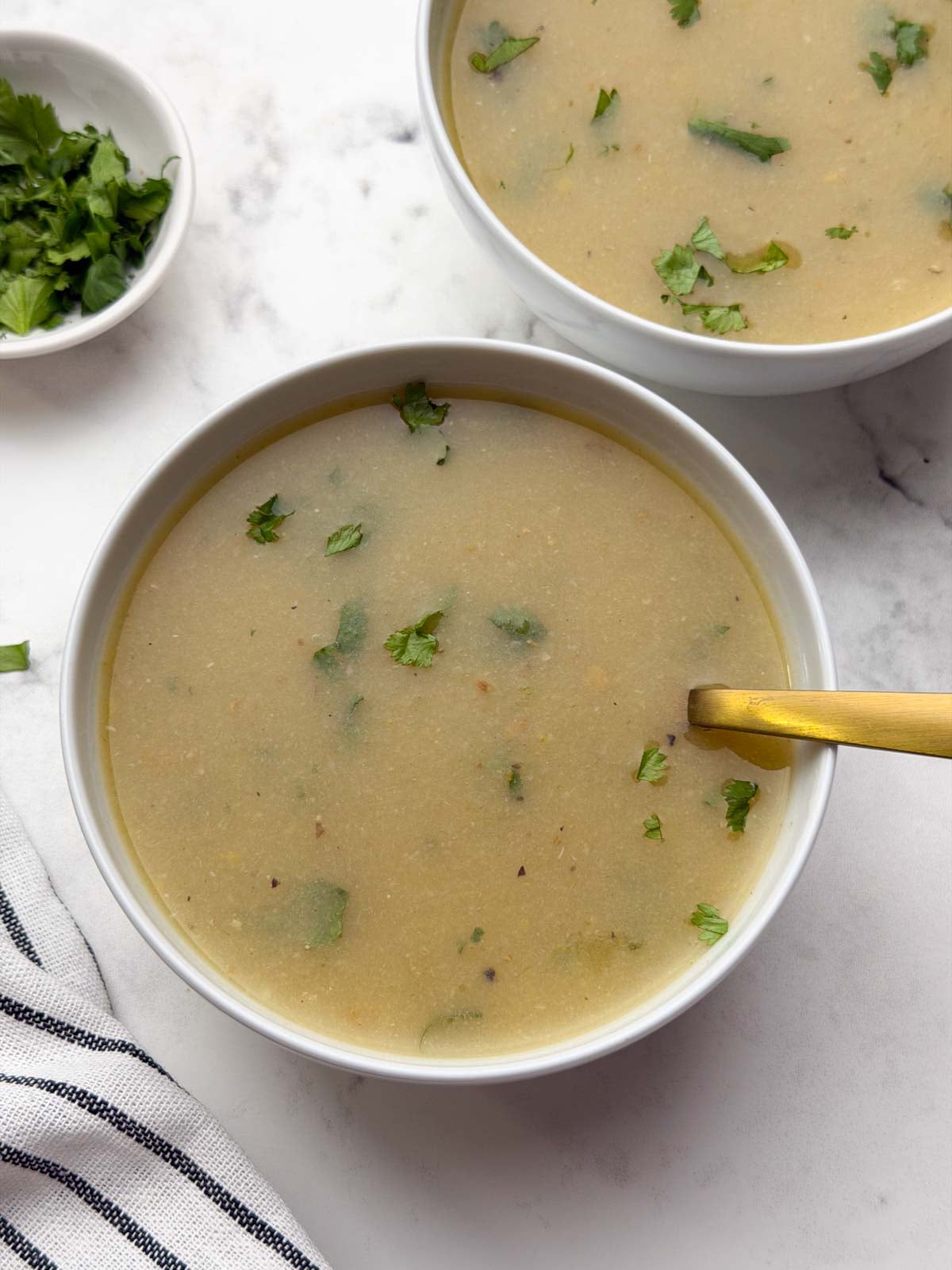 Lauki Monng Dal Soup served in two white bowl with a golden spoon and coriander leaves in a small bowl for garnish.