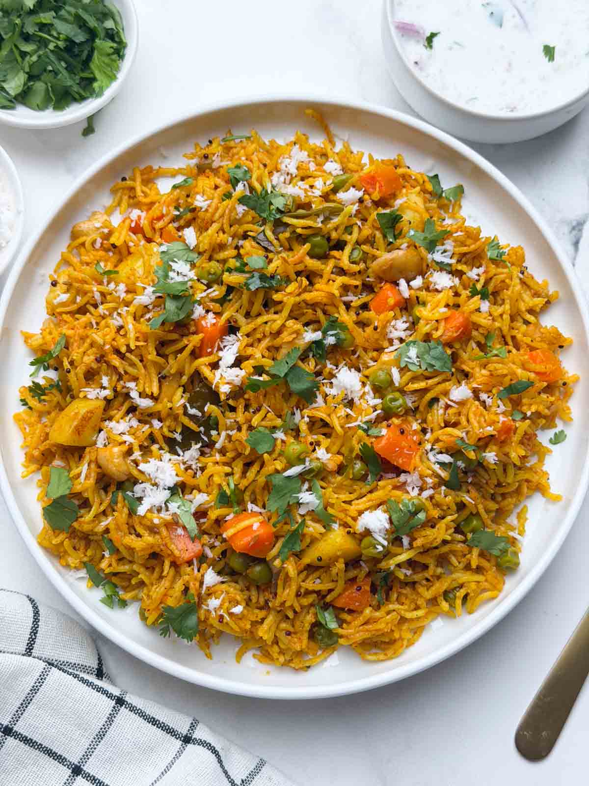 Masale bhaat served in a white plate accompanied by raita in a small bowl and coriander leaves on the side.