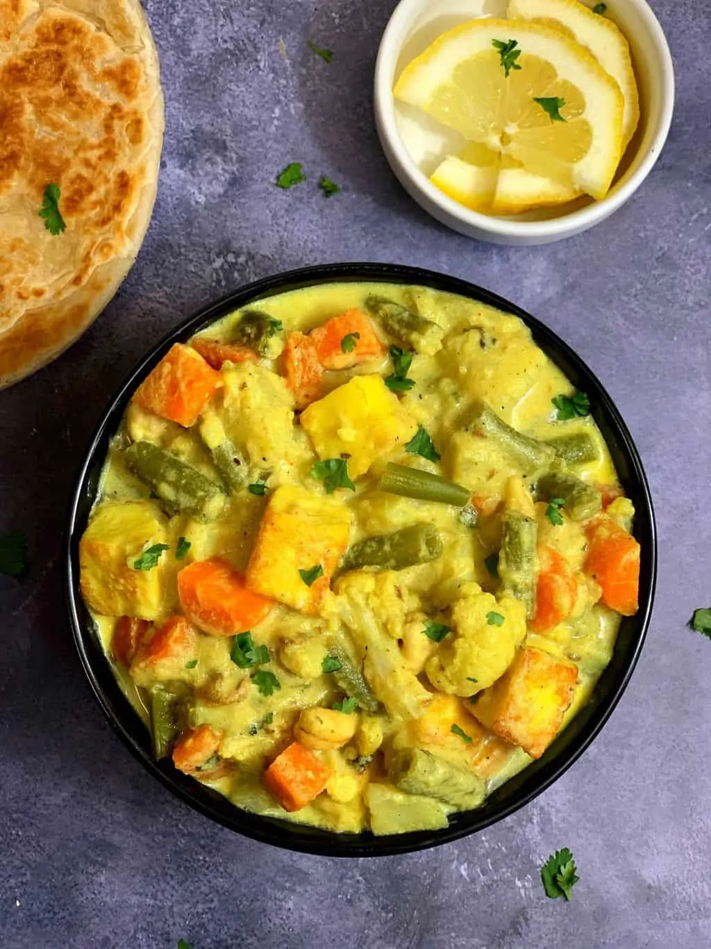 navratan korma curry served in a bowl with lemon wedge and paratha on the side