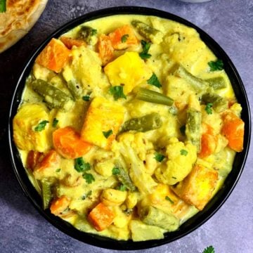 Navratan Korma served in a serving bowl with paratha on the side