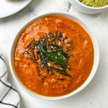 onion tomato chutney served in a bowl with tempering on the top with side of coconut chutney and idli