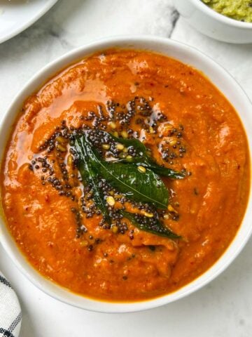 onion tomato chutney served in a bowl with tempering on the top with side of coconut chutney and idli