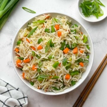 veg fried rice in a bowl with chopped spring onions and chop sticks on the side.