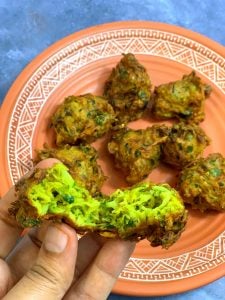 zucchini pakodas on a plate and one pakoda split into half.