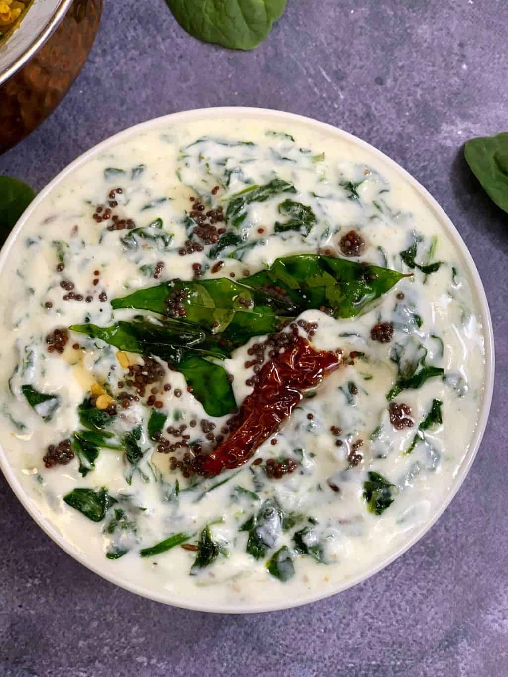 spinach (palak) raita recipe served in a bowl with tempering on the top