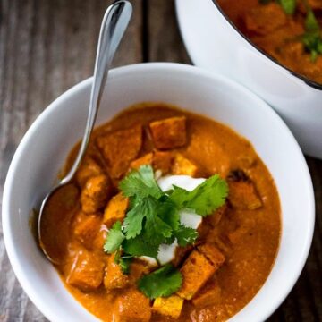 Butternut tikka masala served in a bowl garnished with cilantro with a spoon in it and on the side dutch oven with butternut tikka masala.