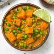 butternut squash coconut curry served in a bowl with lime wedge on top and cooked basmati rice on the side