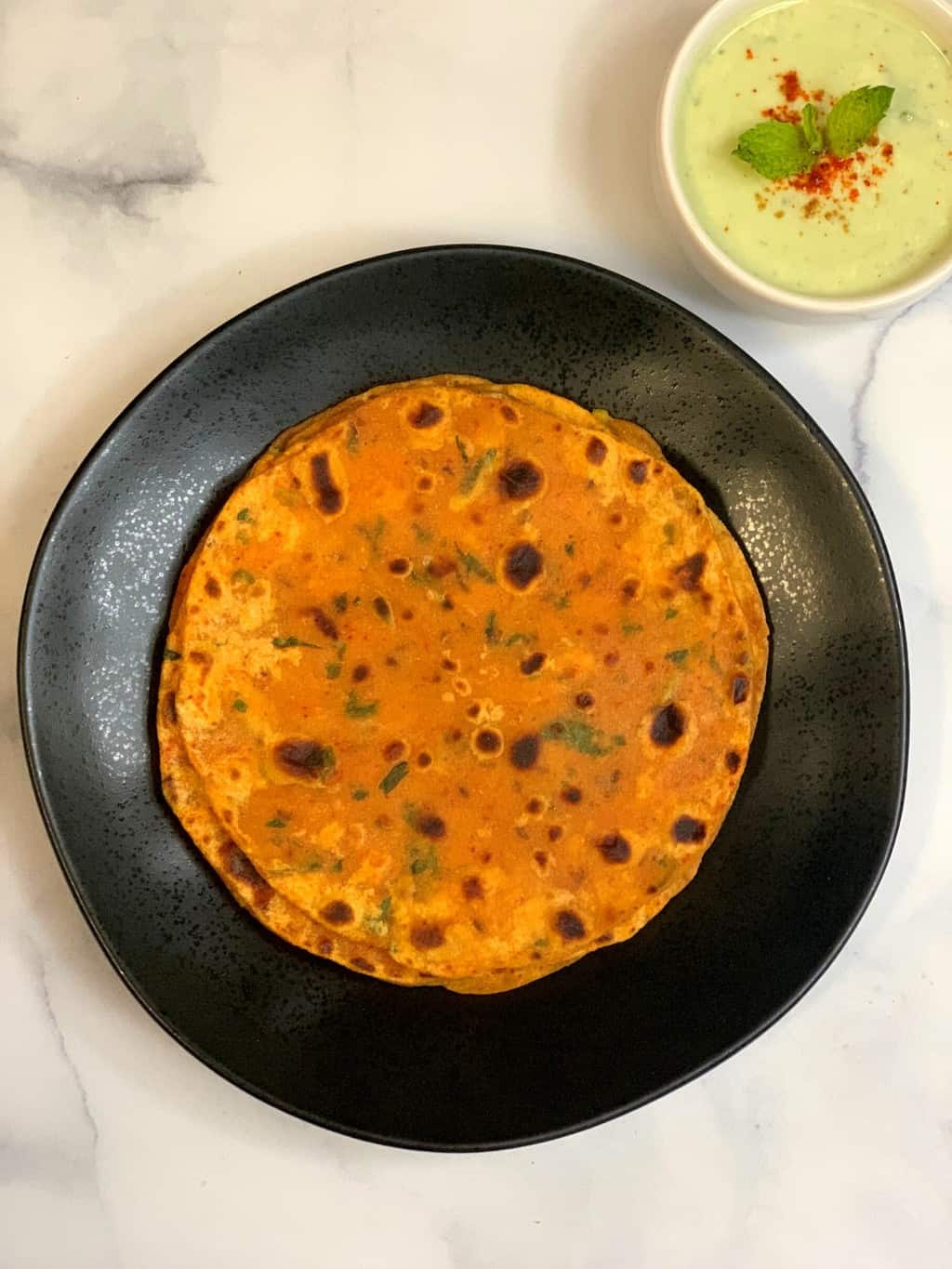 butternut squash paratha in a black plate with mint raita on side