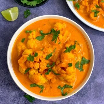 instant pot cauliflower coconut curry served in a white bowl with lemon wedges and cilantro on side