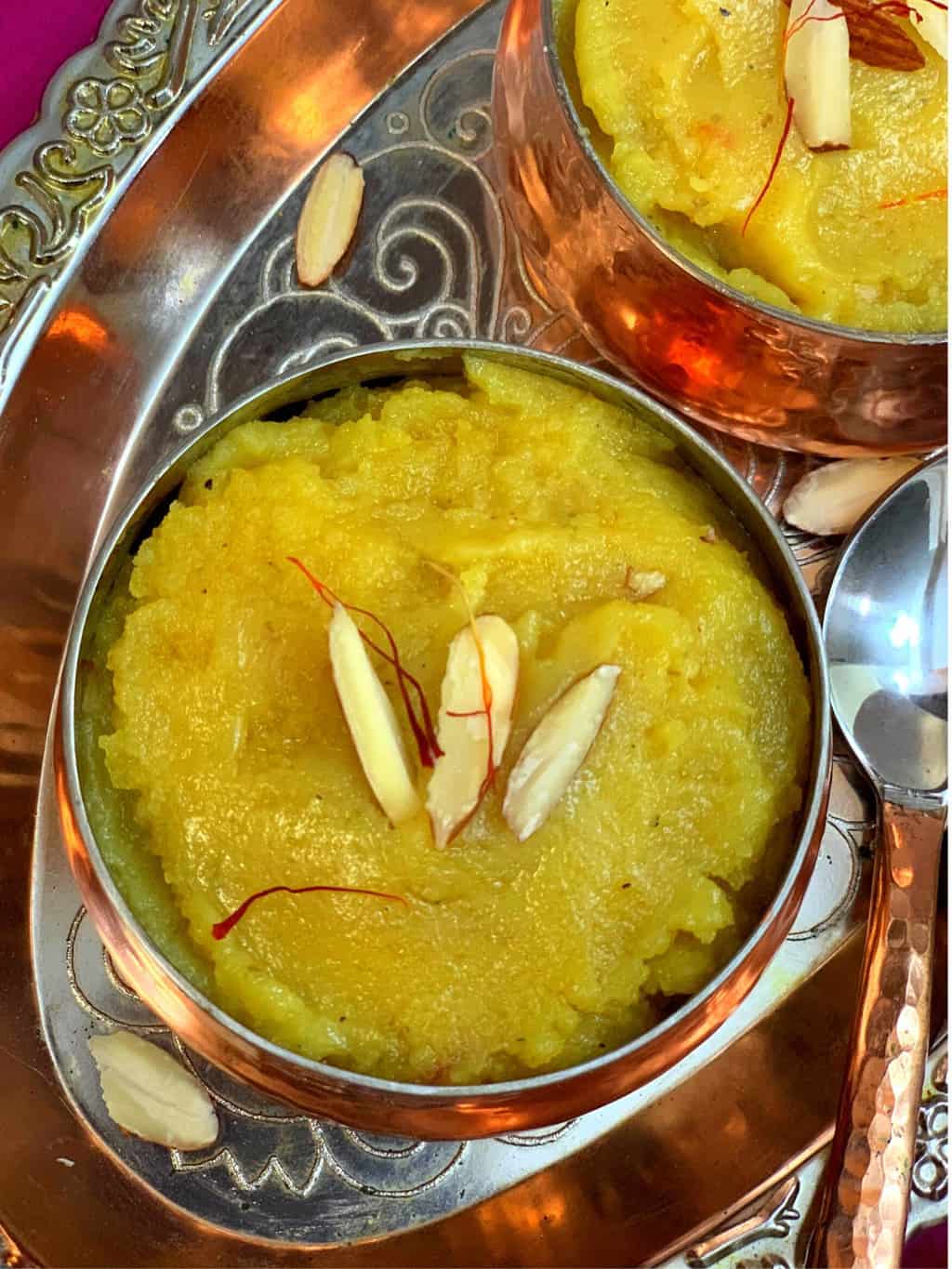 instant pot badam halwa in a copper bowl garnished with saffron and almonswith spoon on side