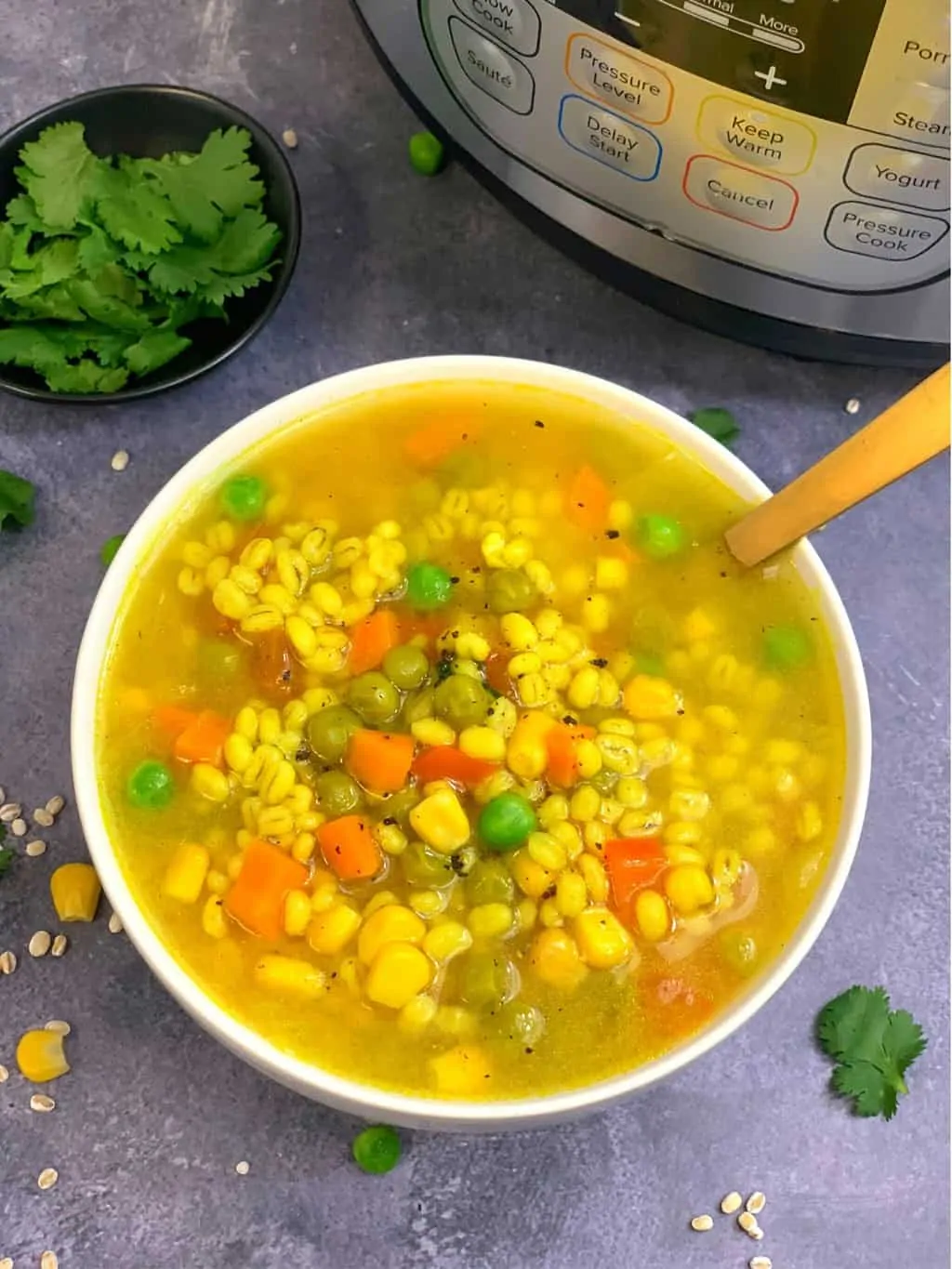 vegetable barley soup in a white bowl with golden spoon and instant pot on side
