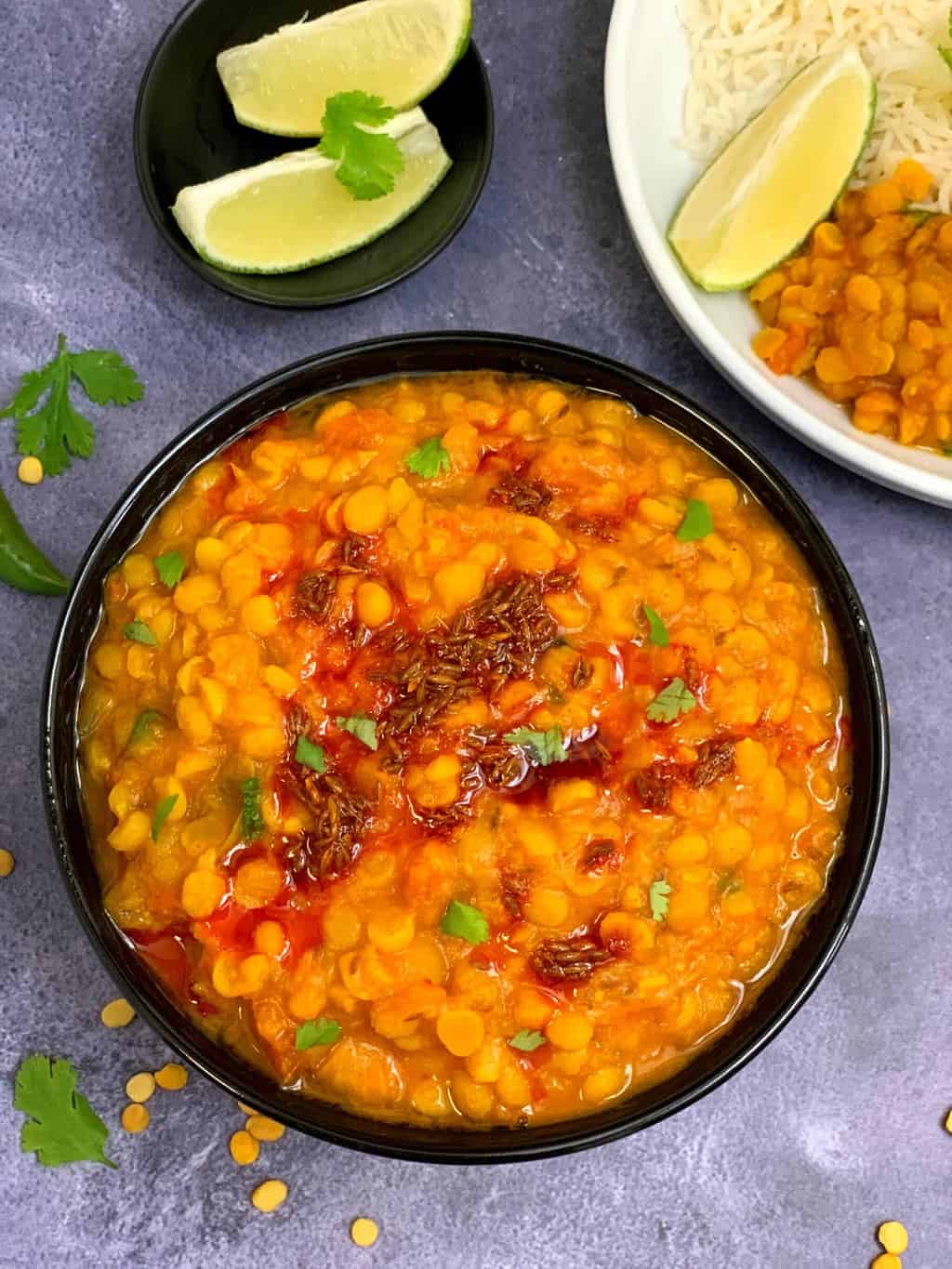 instant pot chana dal serve din a black bowl with lemon wedges on the side