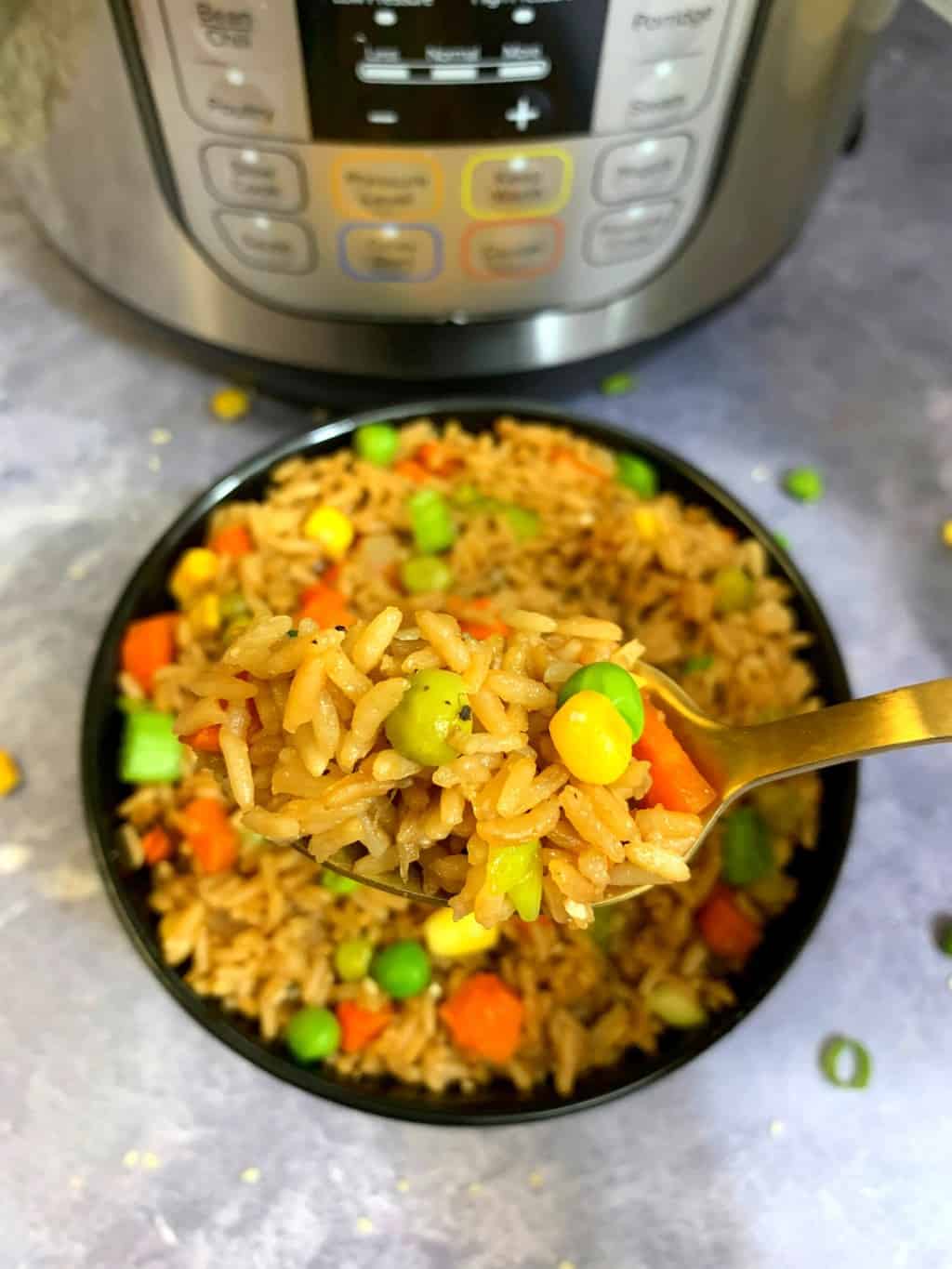 fried rice with vegetables served in a spoon with instant pot on the side