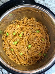 garlic noodles in a instant pot insert garnished with sesame seeds and green onions