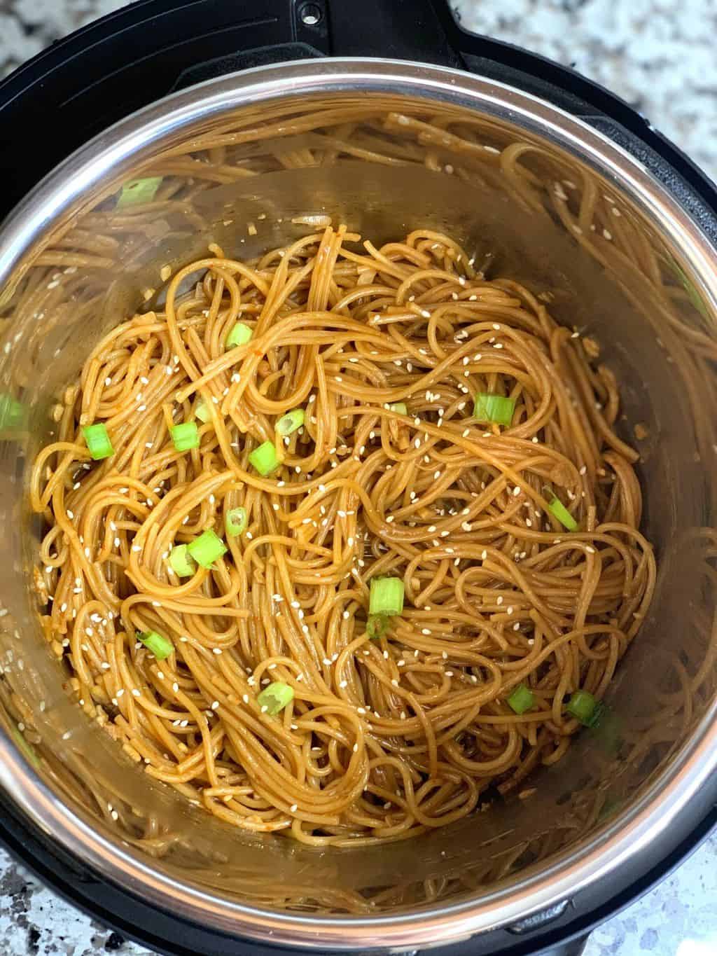 garlic noodles in a instant pot insert garnished with sesame seeds and green onions 