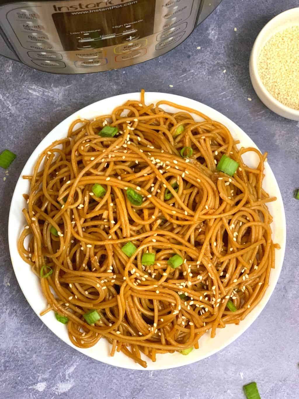 instant pot garlic noodles served in a plate garnished with green onions and instant pot on the side