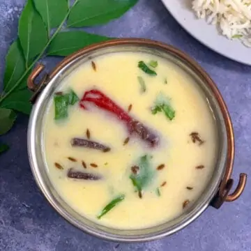 gujarati kadhi in a copper serving bowl with rice and curry leaves on side