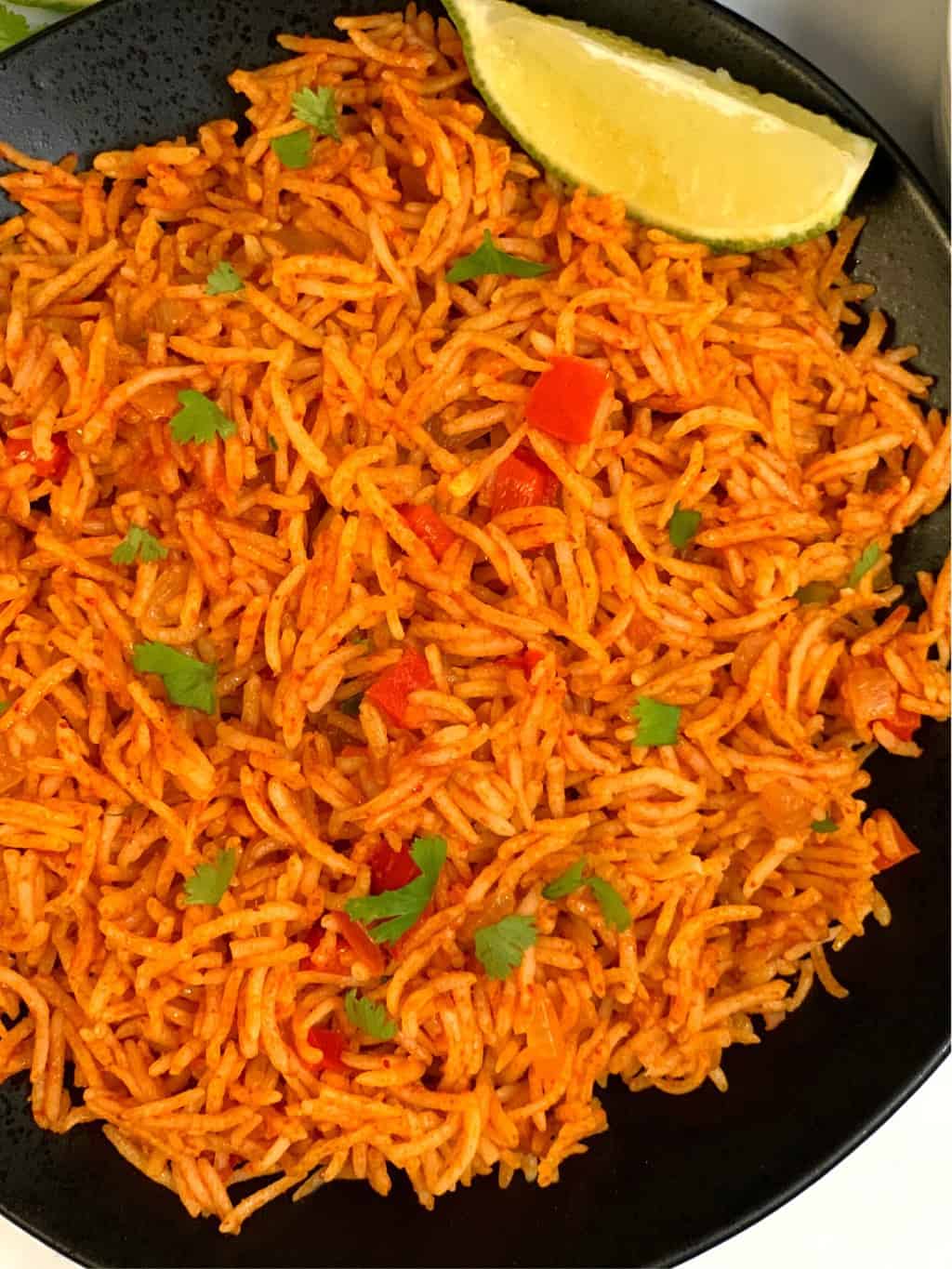 spanish rice served in a plate garnished with cilantro and lemon wedge on the side