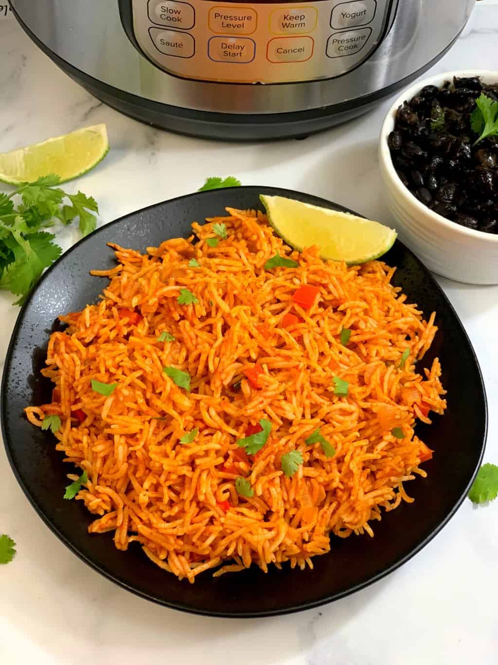 mexican rice served on a plate with cilantro and lemon on top and side of black beans