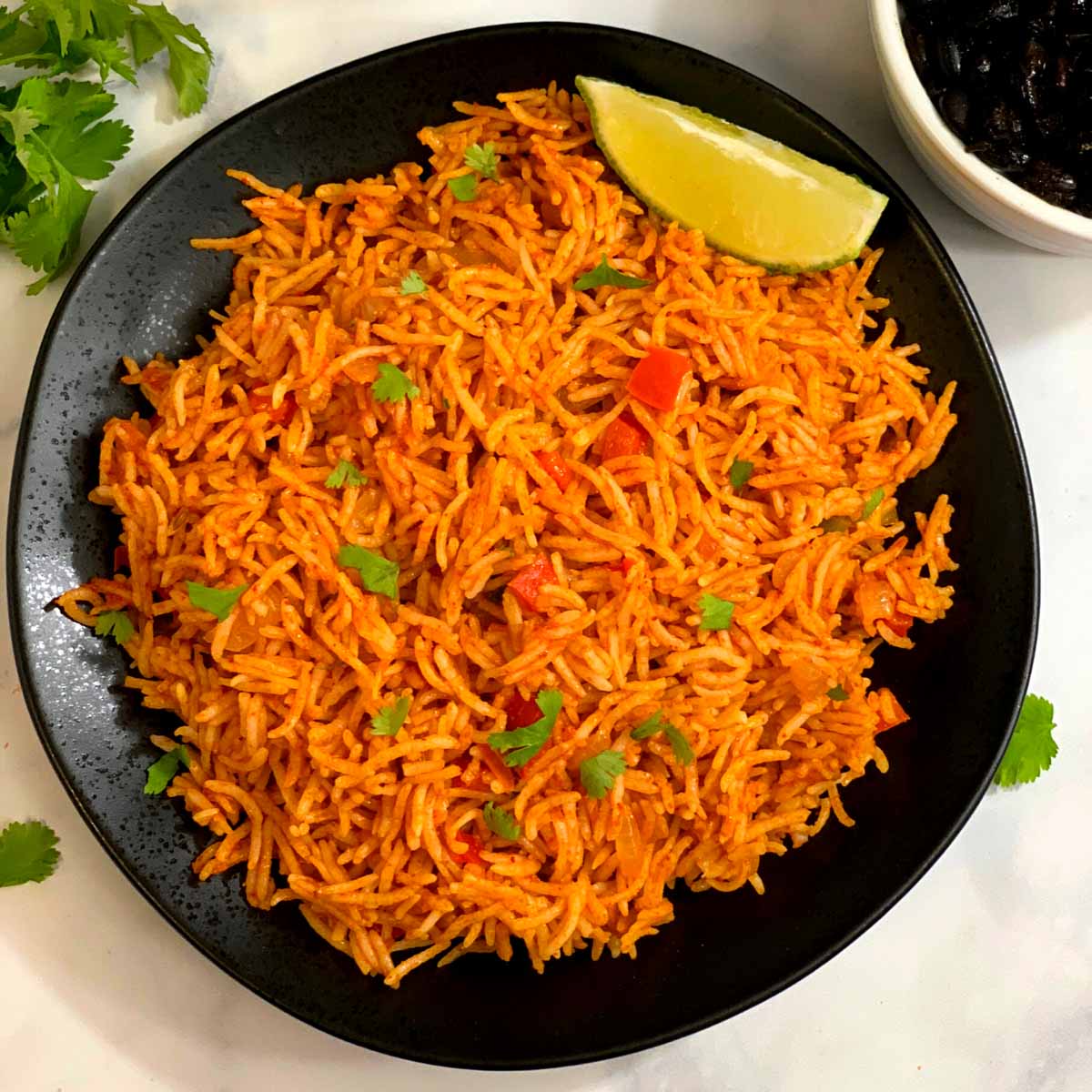 Restaurant style Mexican rice served in a black plate with lemon wedge on top