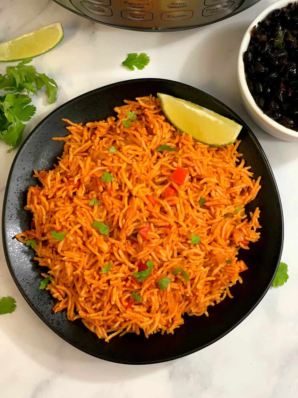 mexican rice served in a black plate with lemon wedge on the side and cooked black beans on the side